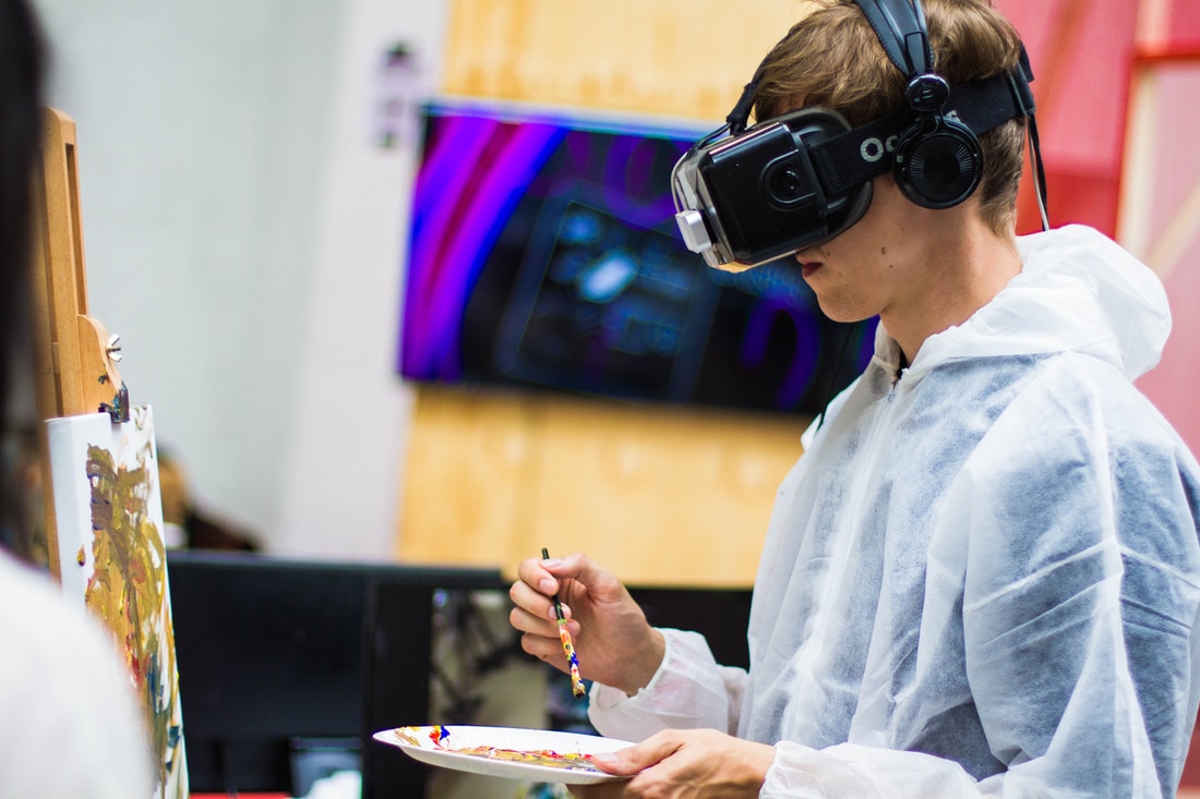 Male student using VR headset and real paint to create image on a canvas
